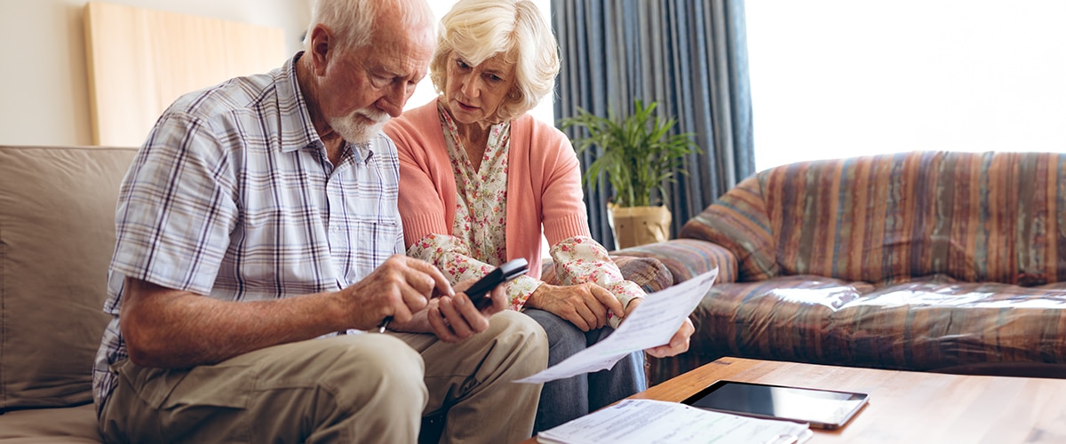 Older couple examining retirement documents with calculator, worried about unexpected tax deductions.