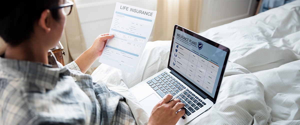Individual comparing multiple income protection policies on laptop with notes about benefits and waiting periods.